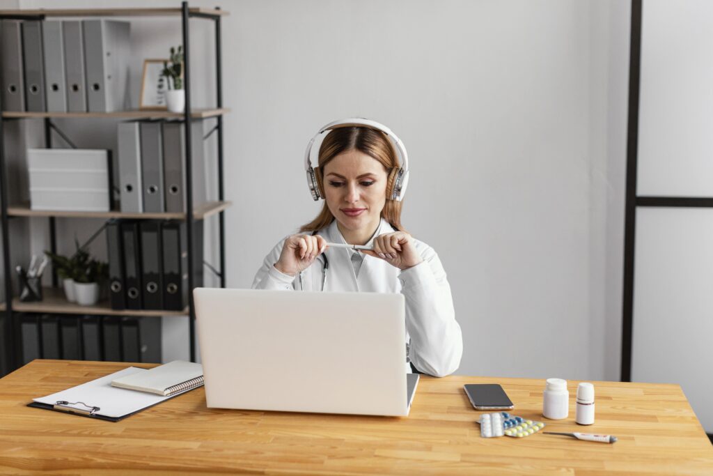 Junge Frau mit Kopfhörern bei der Arbeit am Laptop als virtuelle Assistenz im Homeoffice mit medizinischen Unterlagen
