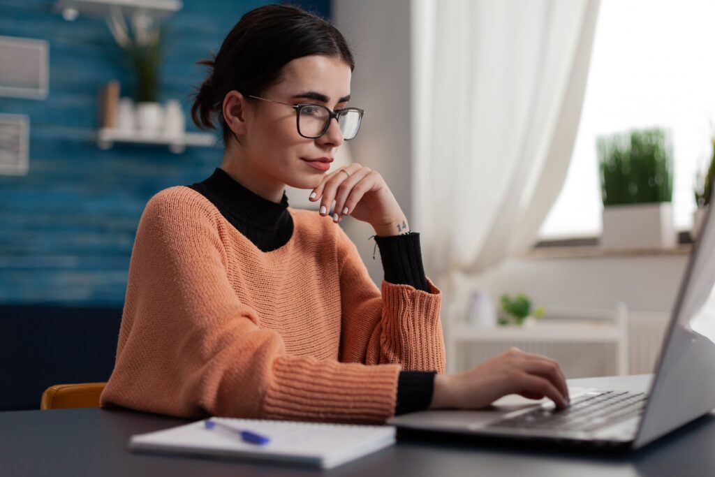 Junge, konzentrierte Frau mit Brille und Pullover, die im Homeoffice am Laptop arbeitet. Symbolbild für effizientes Working with Freelancers im Remote-Team